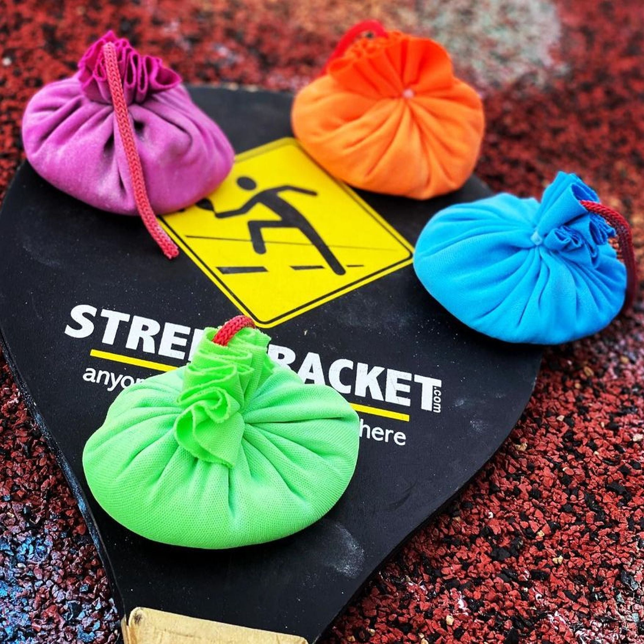 Schwarzes Racket mit 4 bunten Kreidebällen darauf: orange, lila, grün, blau.