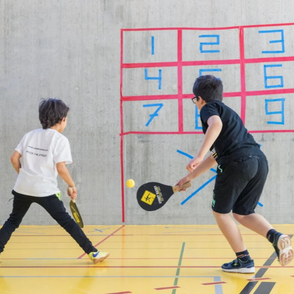 Zwei Kinder führen eine Übung aus dem Street-Racket-Spielfächer aus, ideal für bewegtes Lernen.